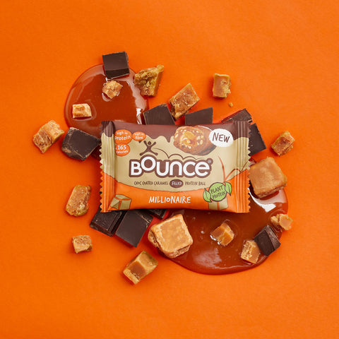 Bounce filled Caramel Millionaire on orange background surrounded by chocolate and caramel chunks and placed on a pool of caramel sauce.