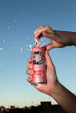 Photo of the side of Dalstons Rasberry Prebiotic Soda 250ml being opened and fizzing everywhere infront of sunset city-scape.