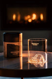Gilded Peaks Helvellyn Glass tumbler and coaster set shown with the box from the front, in front of a fire