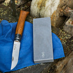 Sharpeming stone next to opinel knife on a outdoor wooden surface.
