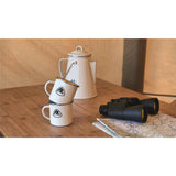 Robens Tongass Enamel Kettle on a table with enamel mugs and a map and pair of binoculars