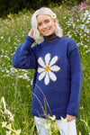 Pachamama Daisy Sweater in Denim showing a model in a feild of daisies and with a daisy shoved alluringly behind her left ear just to add to the general daisiness of the scene.