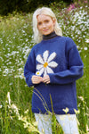 Pachamama Daisy Sweater in Denim showing a model in a field of daisies playing with a daisy between her fingers