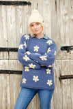 Pachamama Flower Power Sweater in Denim colour with white and yellow daisy designs on blond model wearing a white bobble hat while folding her arms but not looking tough.