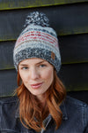 Pachamama Langtang Bobble Beanie in Red. A red, blue and white striped bobble beanie worn by a female model